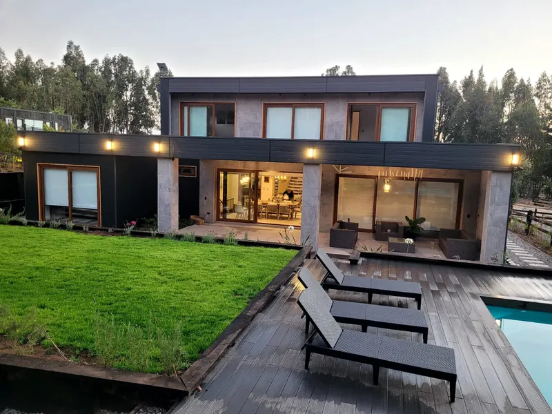 La misma vivienda terminada, con pasto, deck, terraza techada e iluminación exterior