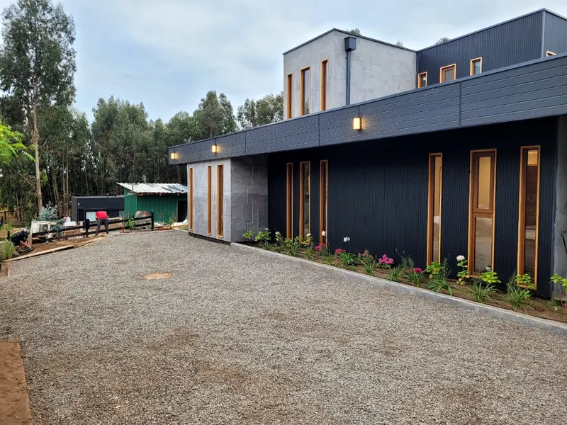 Fachada con revestimiento oscuro, piedra gris y ventanas con marco de madera